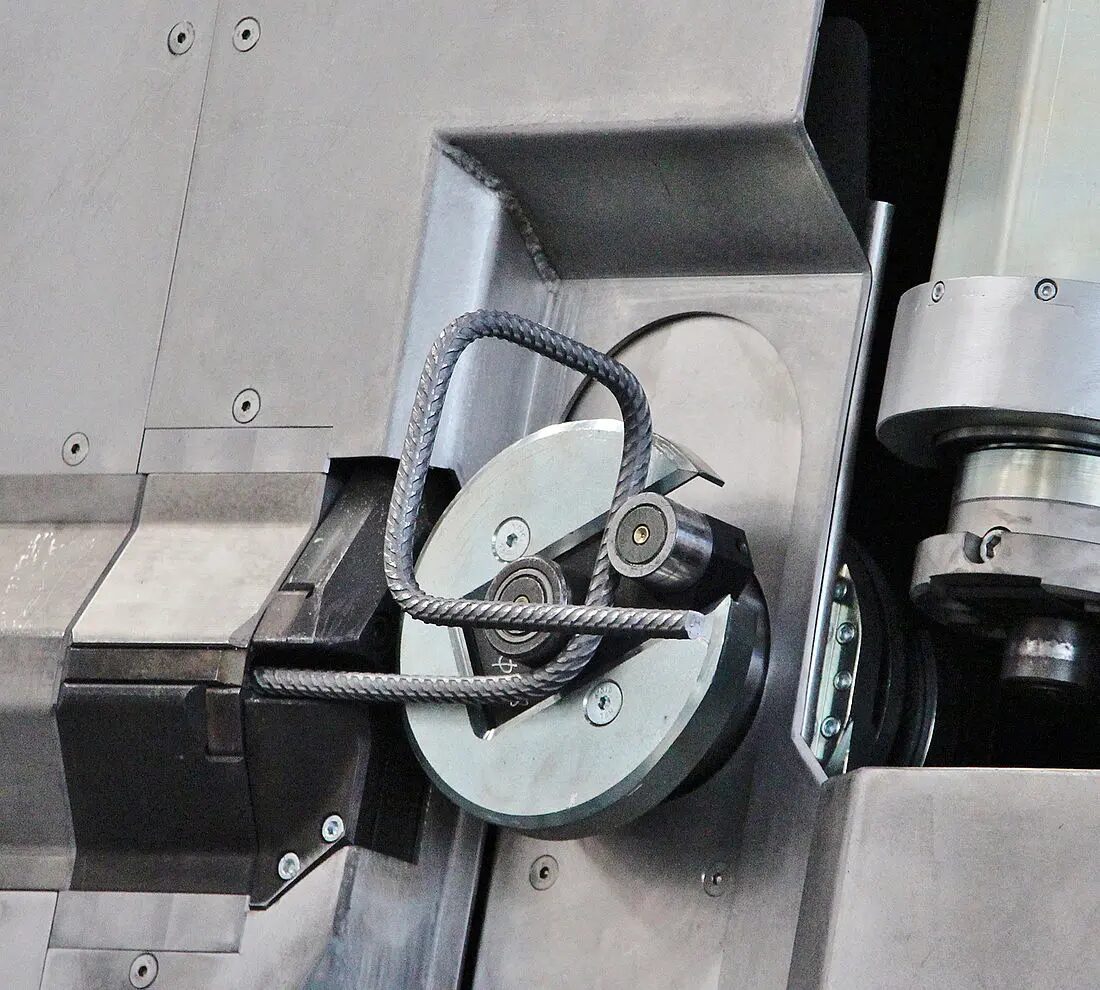 Reinforcement bending machines in a factory environment, showing automated shaping of steel bars according to predefined bending schedules.