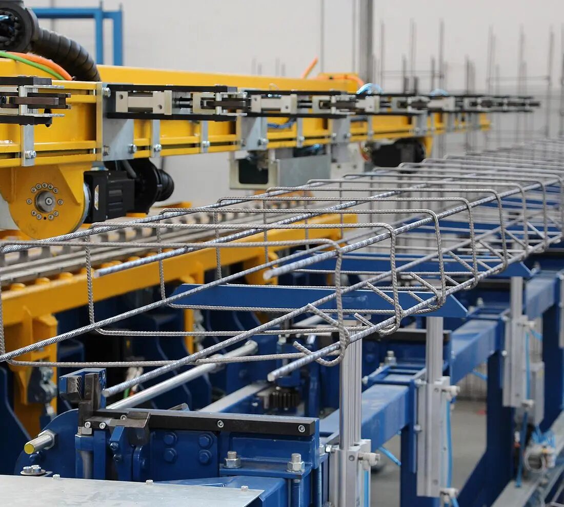 Understanding rebar fabrication through automated bending machines, showing how steel bars are shaped in a factory environment according to fabrication standards.